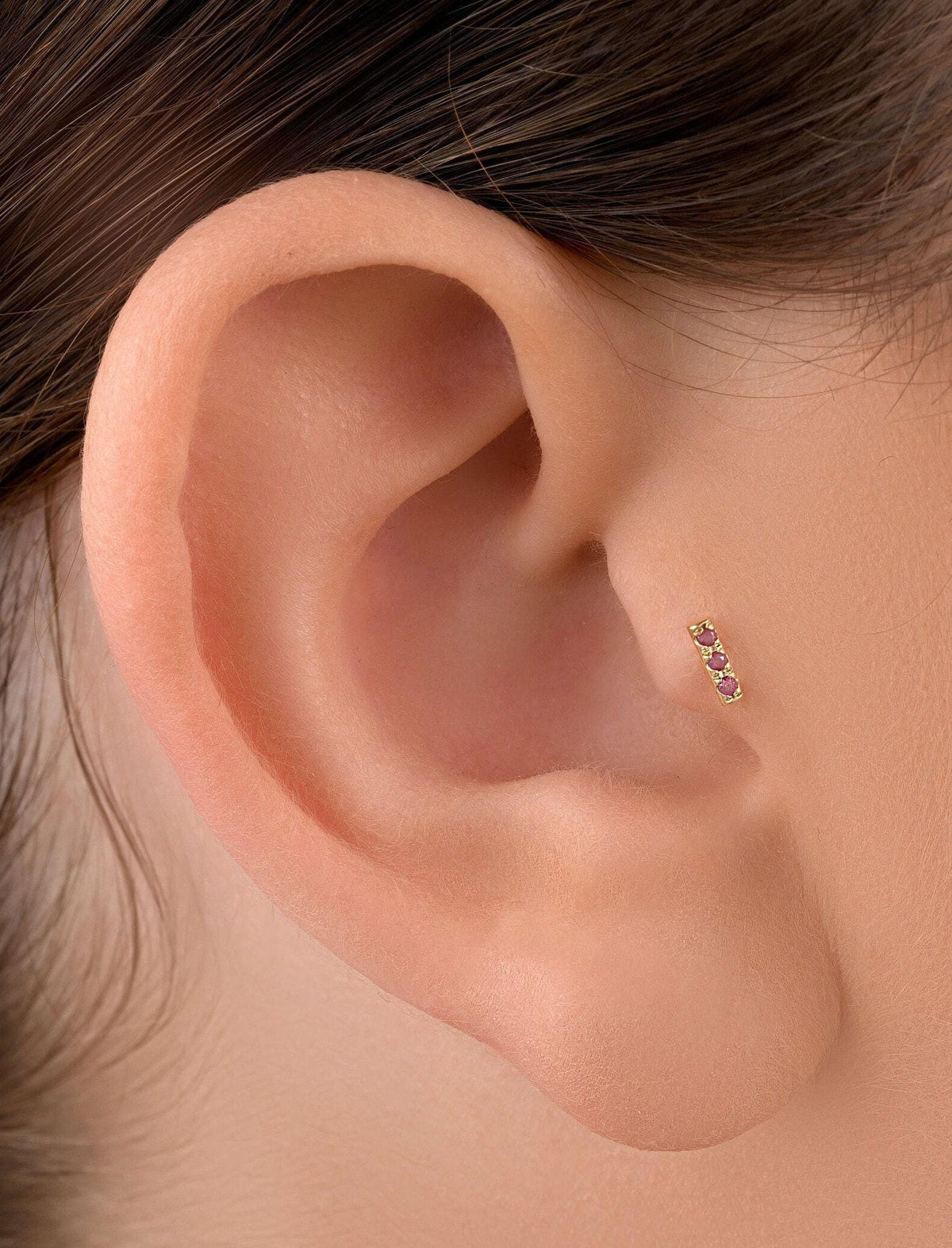 A close-up view of a person's ear, showing a small gold earring with a small gemstone in the earlobe.