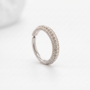 A silver ring with a textured design, featuring a row of small, round stones or dots arranged in a decorative pattern.