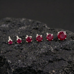 A collection of red gemstone earrings is displayed on a dark surface, with the largest earrings positioned in the center and the smaller ones arranged around them.