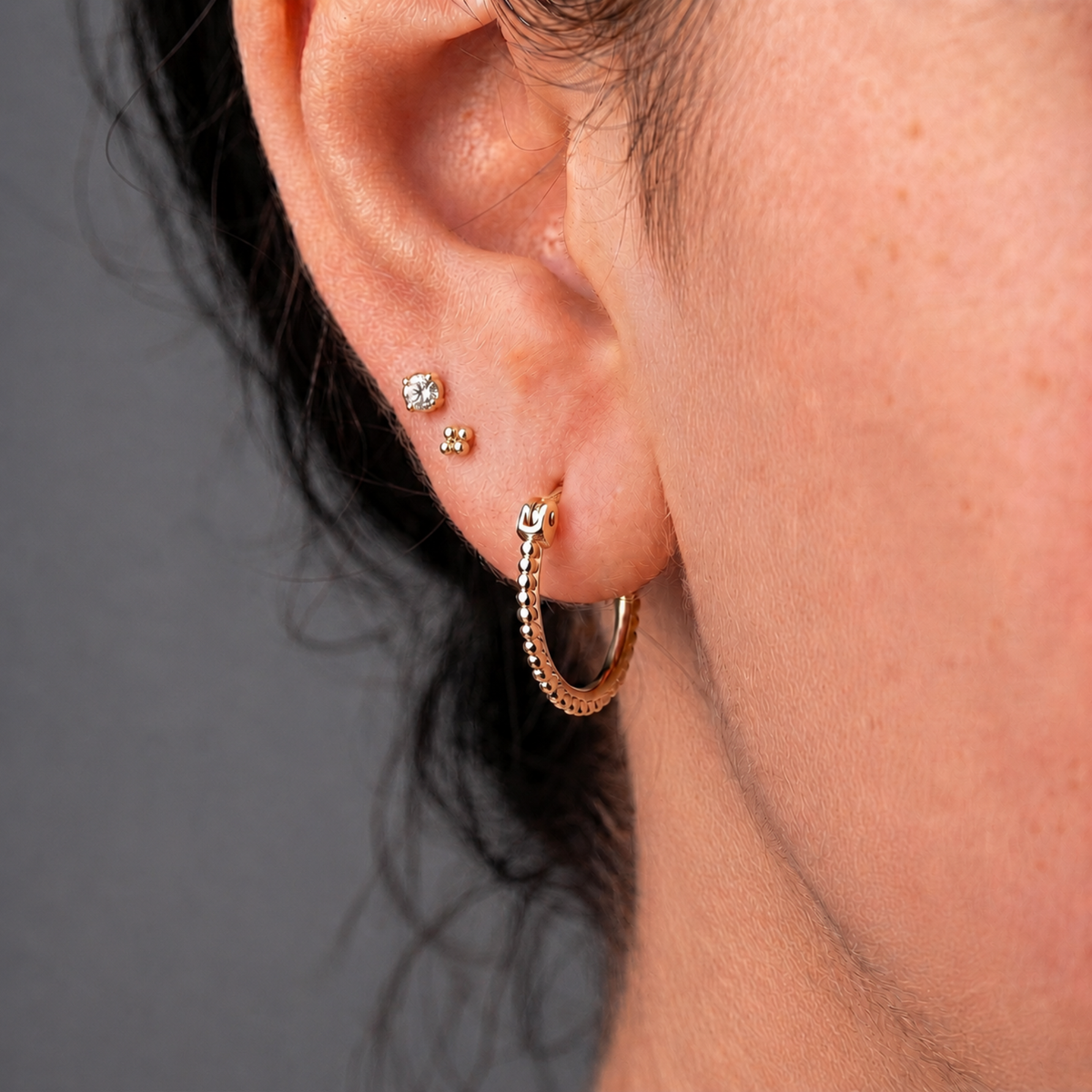 A close-up view of a person's ear adorned with two gold hoop earrings, one on each side of the earlobe.
