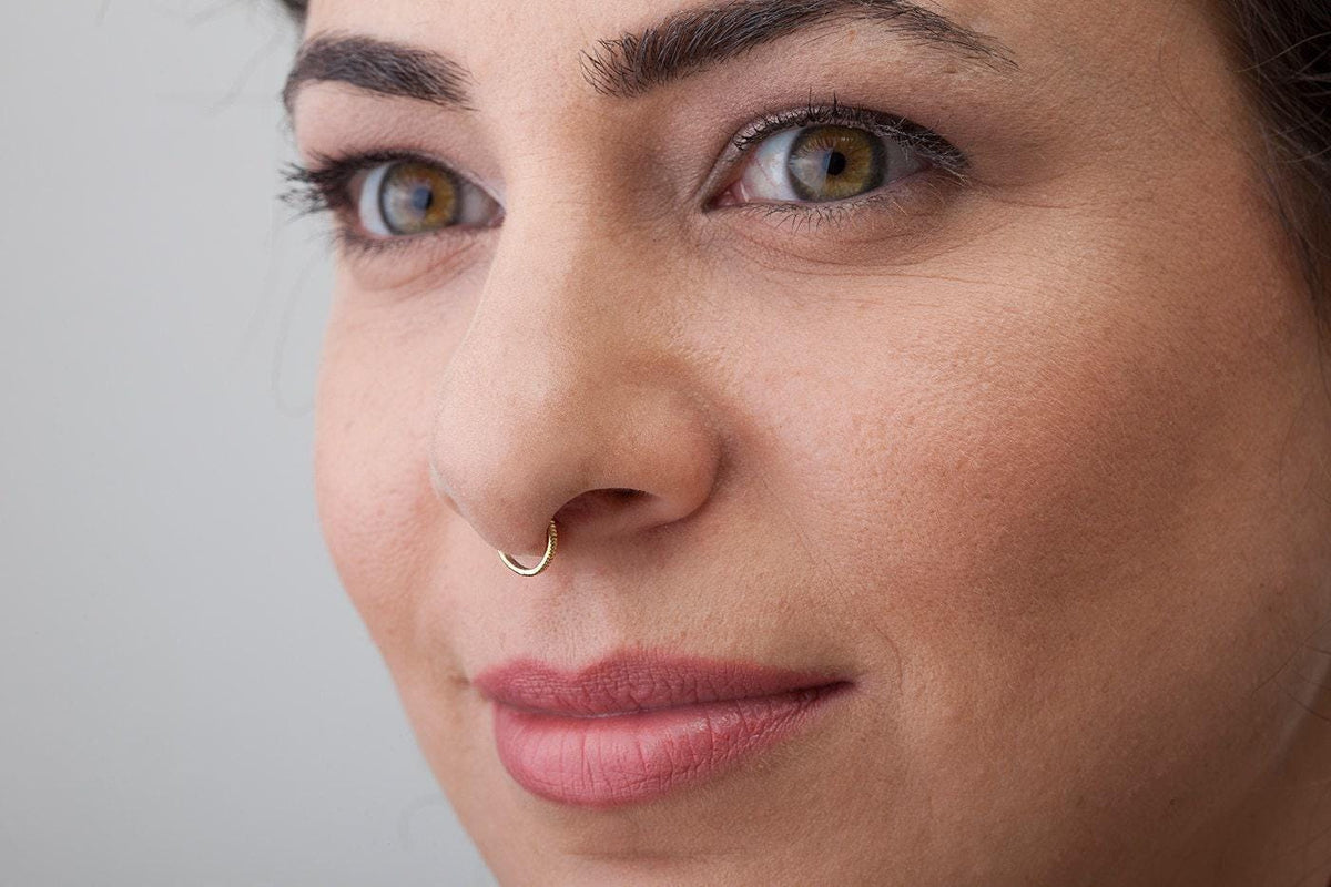 A close-up of a woman's face, focusing on her nose and lips, with a piercing in her nose.