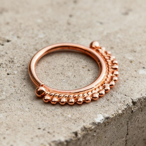 A copper-colored ring with a decorative band of small balls or beads around the edge, resting on a concrete surface.