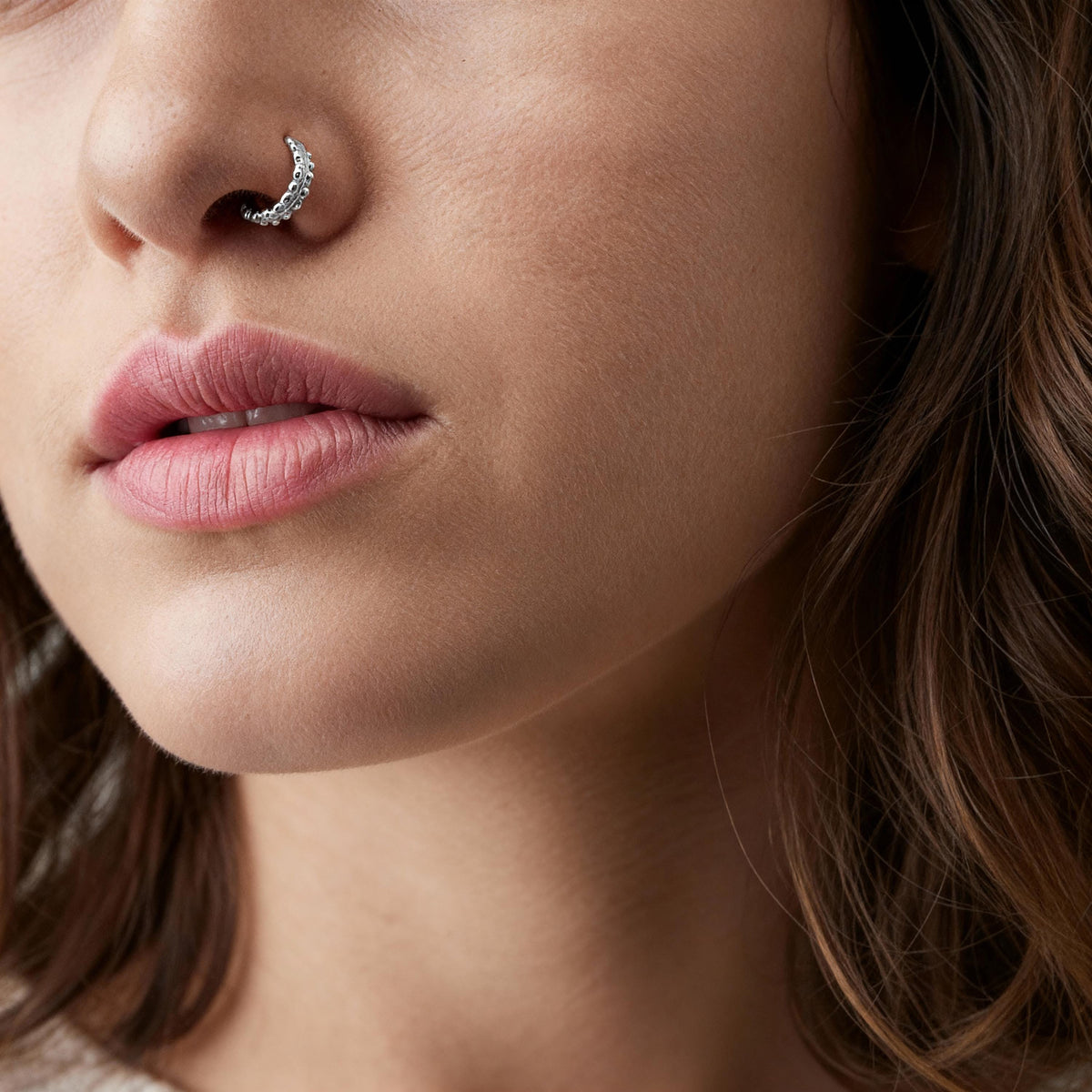 A close-up of a woman's face, focusing on her nose and lips, with a nose ring and a small piece of jewelry visible.