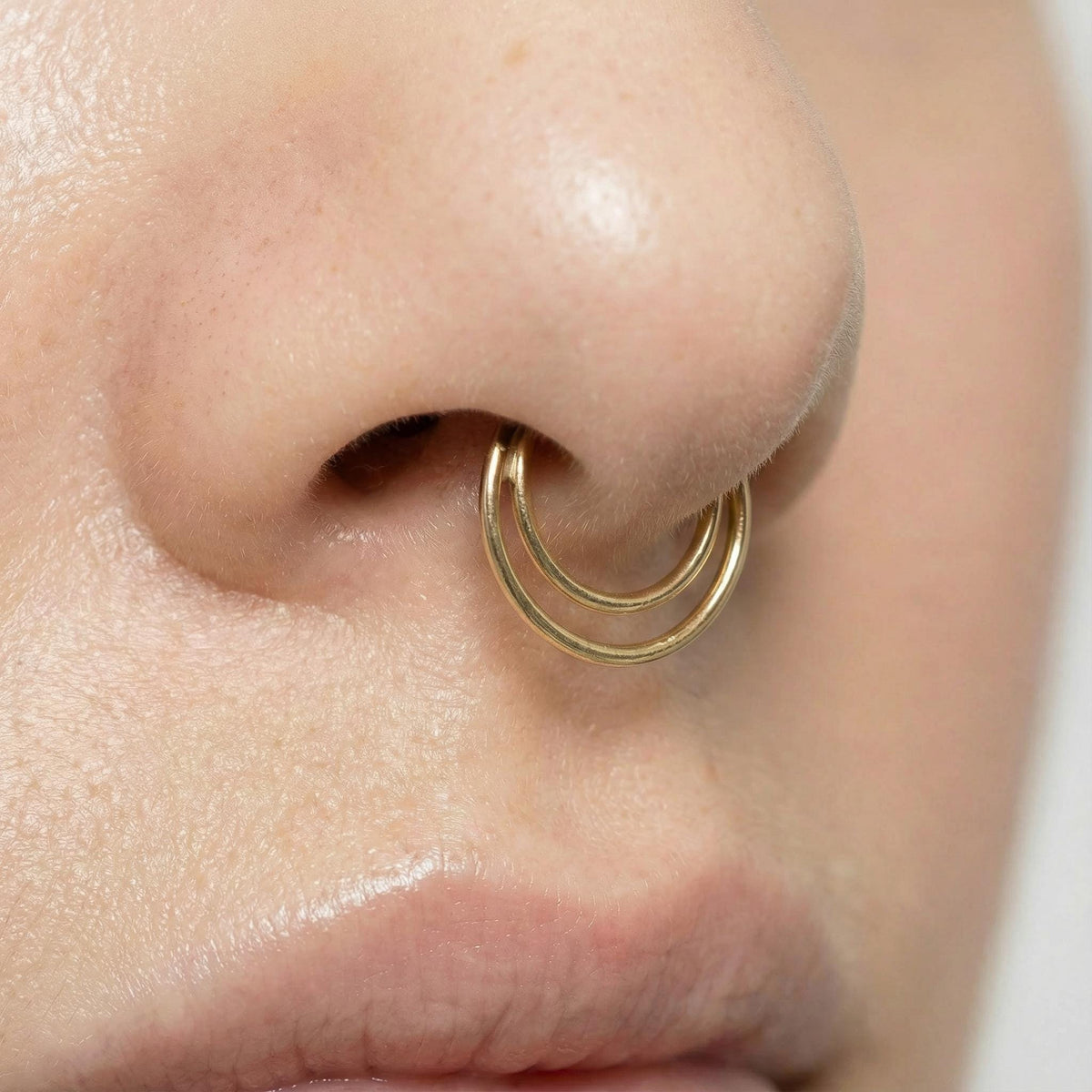 A close-up of a person's nose and mouth, with a gold-colored nose ring visible.