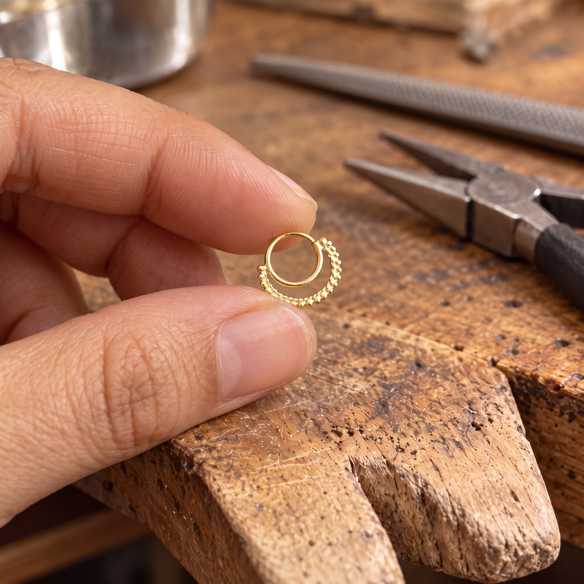 A hand is holding a small gold-colored ring with a spiral design on a wooden workbench.