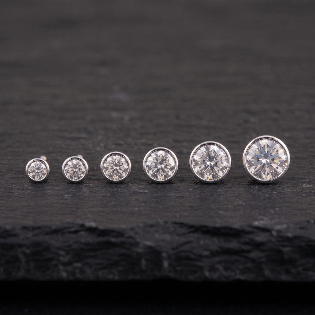 A row of six diamond earrings with varying sizes, all set against a dark background.