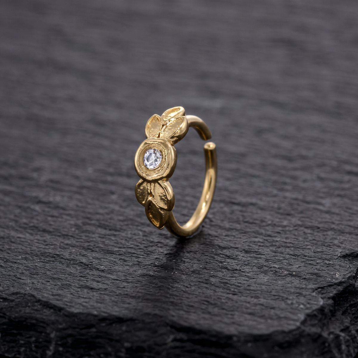 A gold earring with a small diamond in the center is displayed on a dark surface.