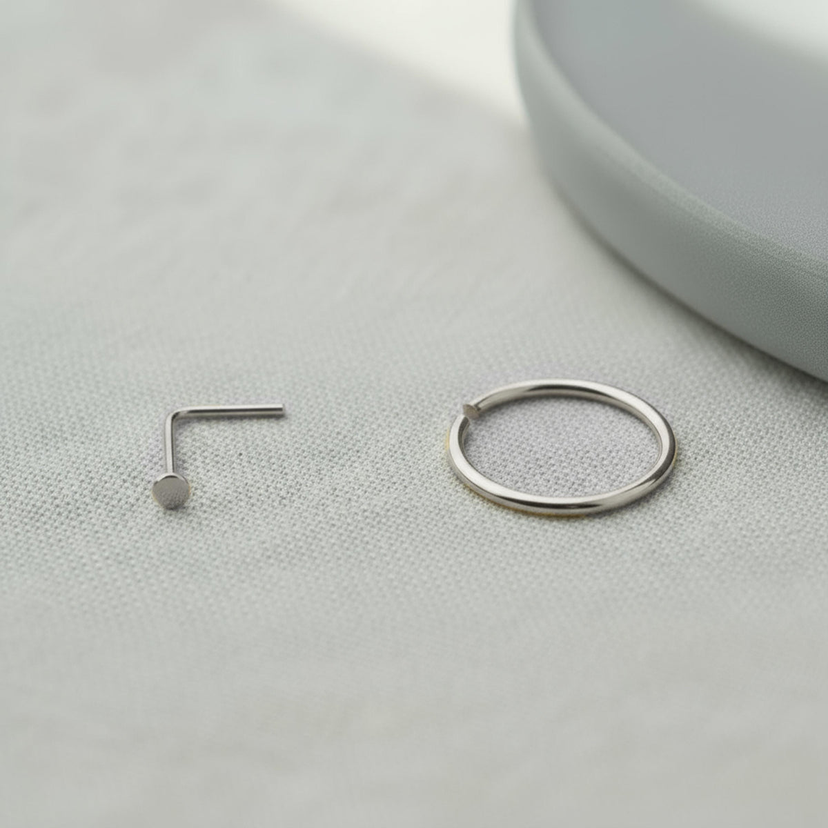 A silver nose ring and a silver ring are placed on a white surface.