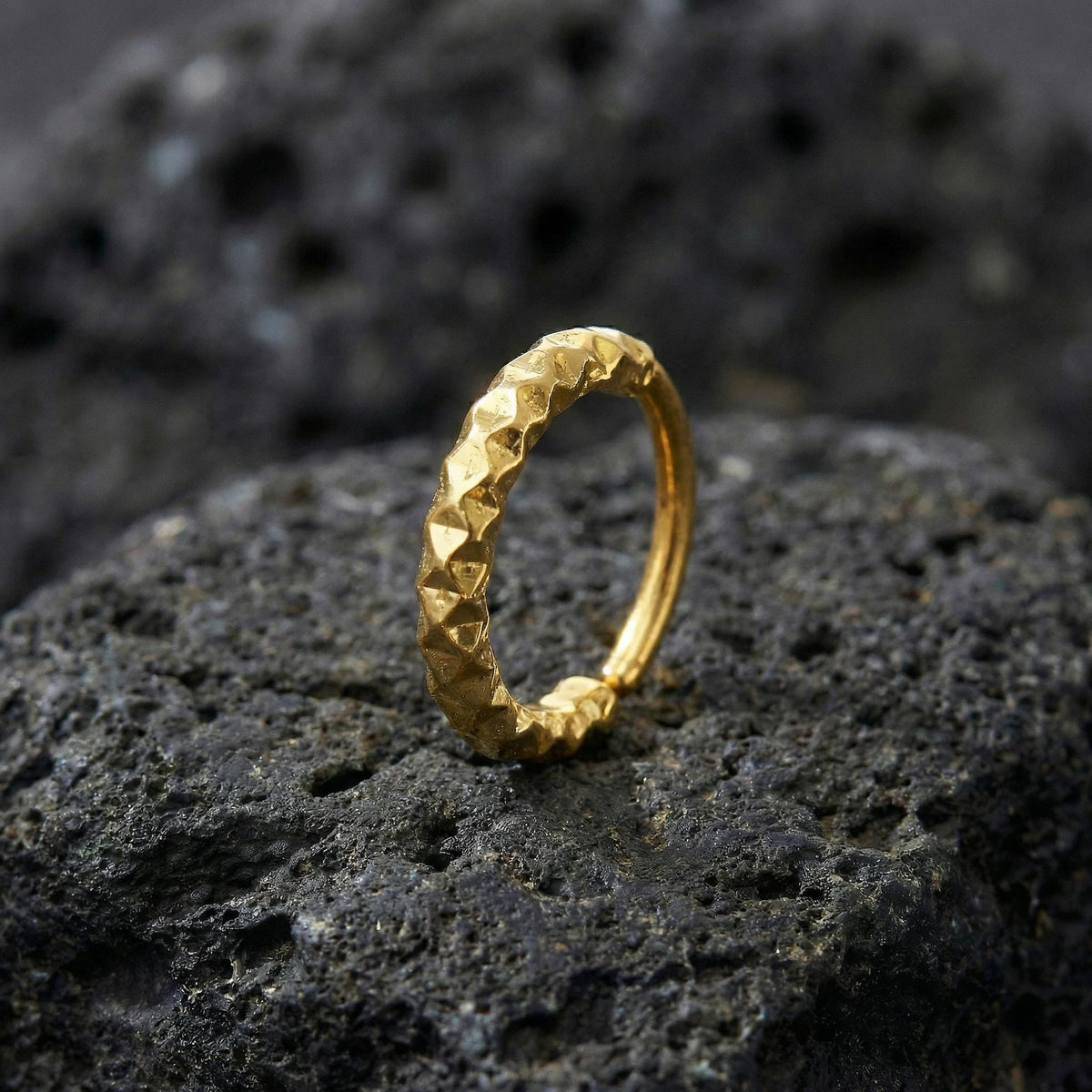 A gold ring with a diamond-like texture sits on a dark, rocky surface.