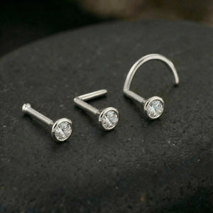 Three white gold nose piercings with diamonds are displayed on a dark surface.