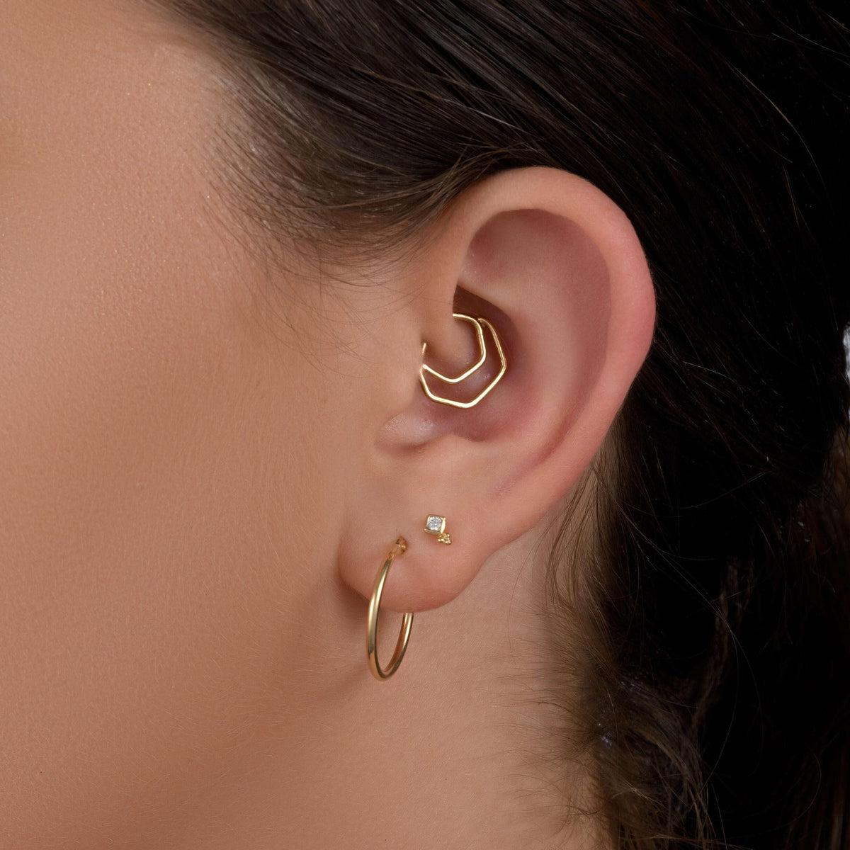 A close-up of a person's ear with a gold hoop earring and a small diamond earring.