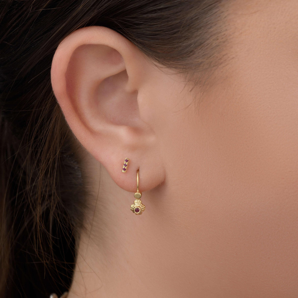 A close-up view of a person's ear adorned with a pair of gold earrings, featuring a small floral charm.