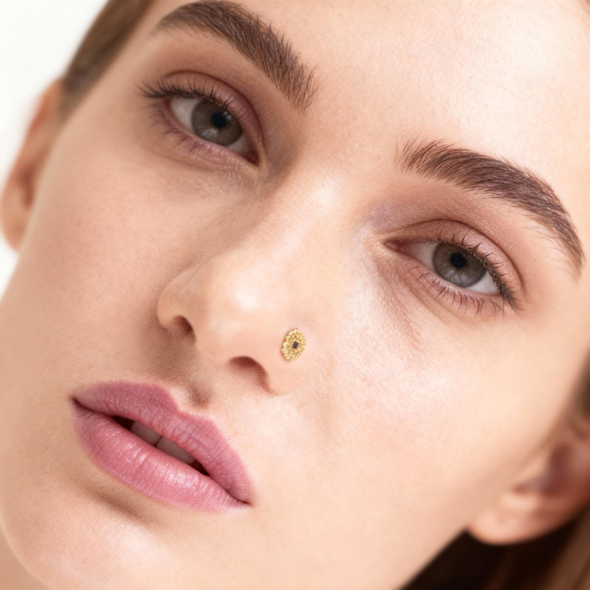 A close-up portrait of a woman with a nose piercing, looking directly at the camera with a neutral expression.