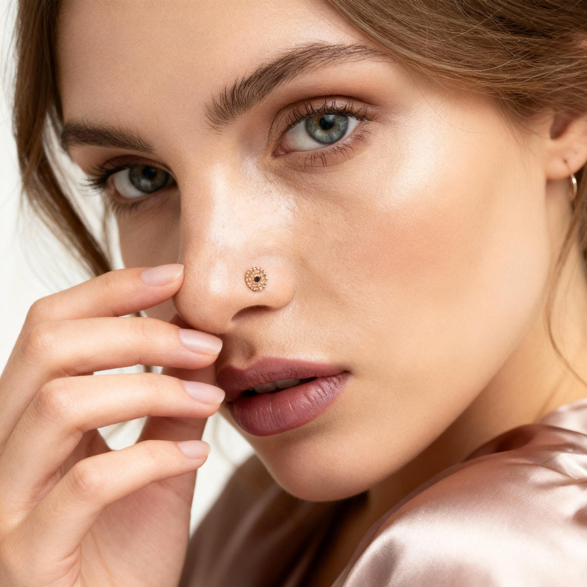 A close-up portrait of a woman with a nose stud, her eyes gazing directly at the camera.