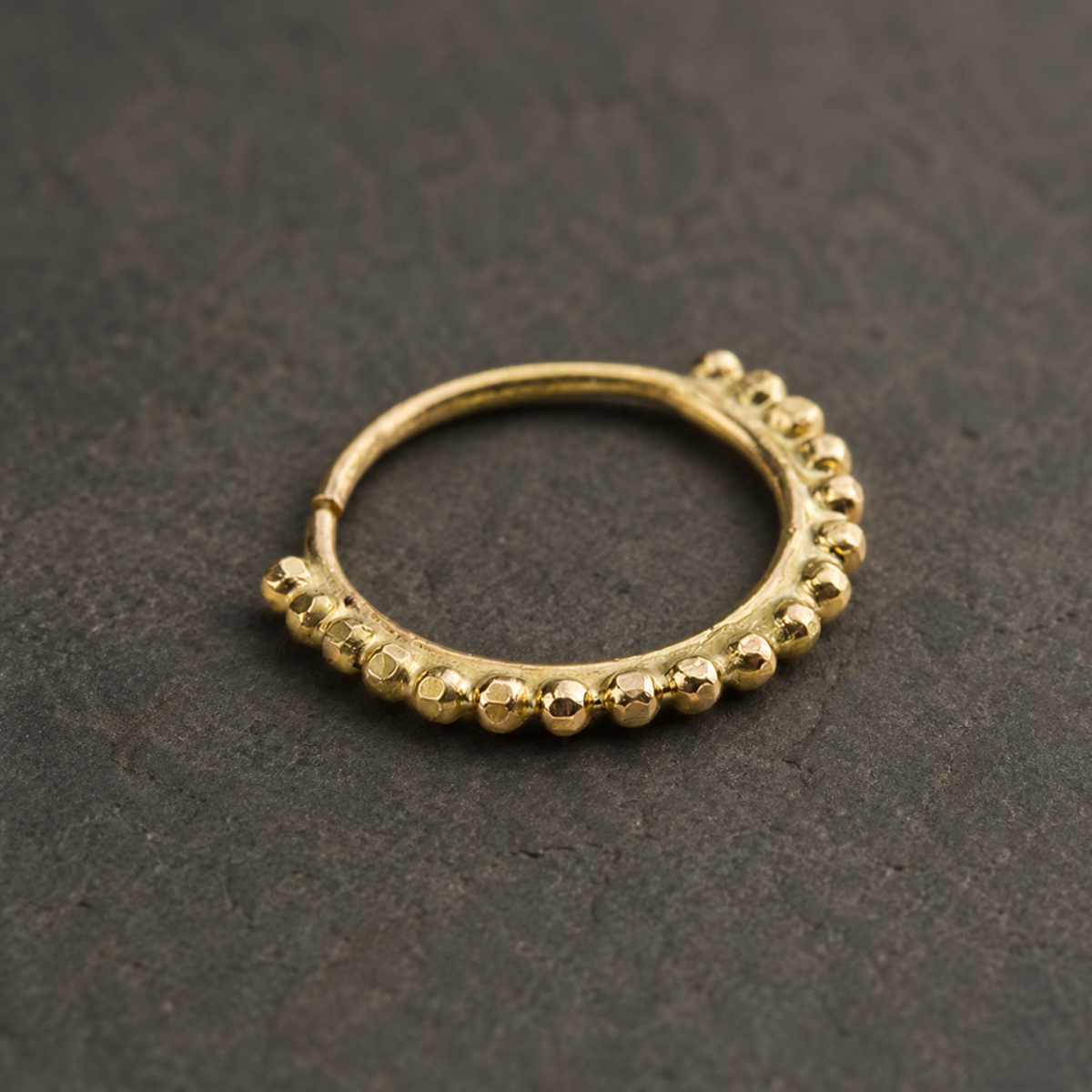 A gold-colored metal ring with a row of small, round, shiny balls or stones along the edge.