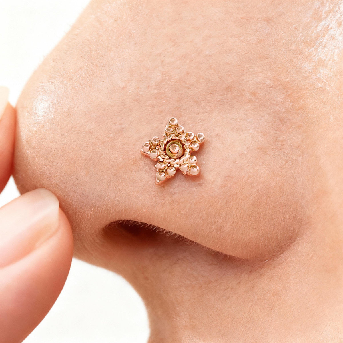 A close-up of a person's nose with a small, ornate gold star-shaped piercing.