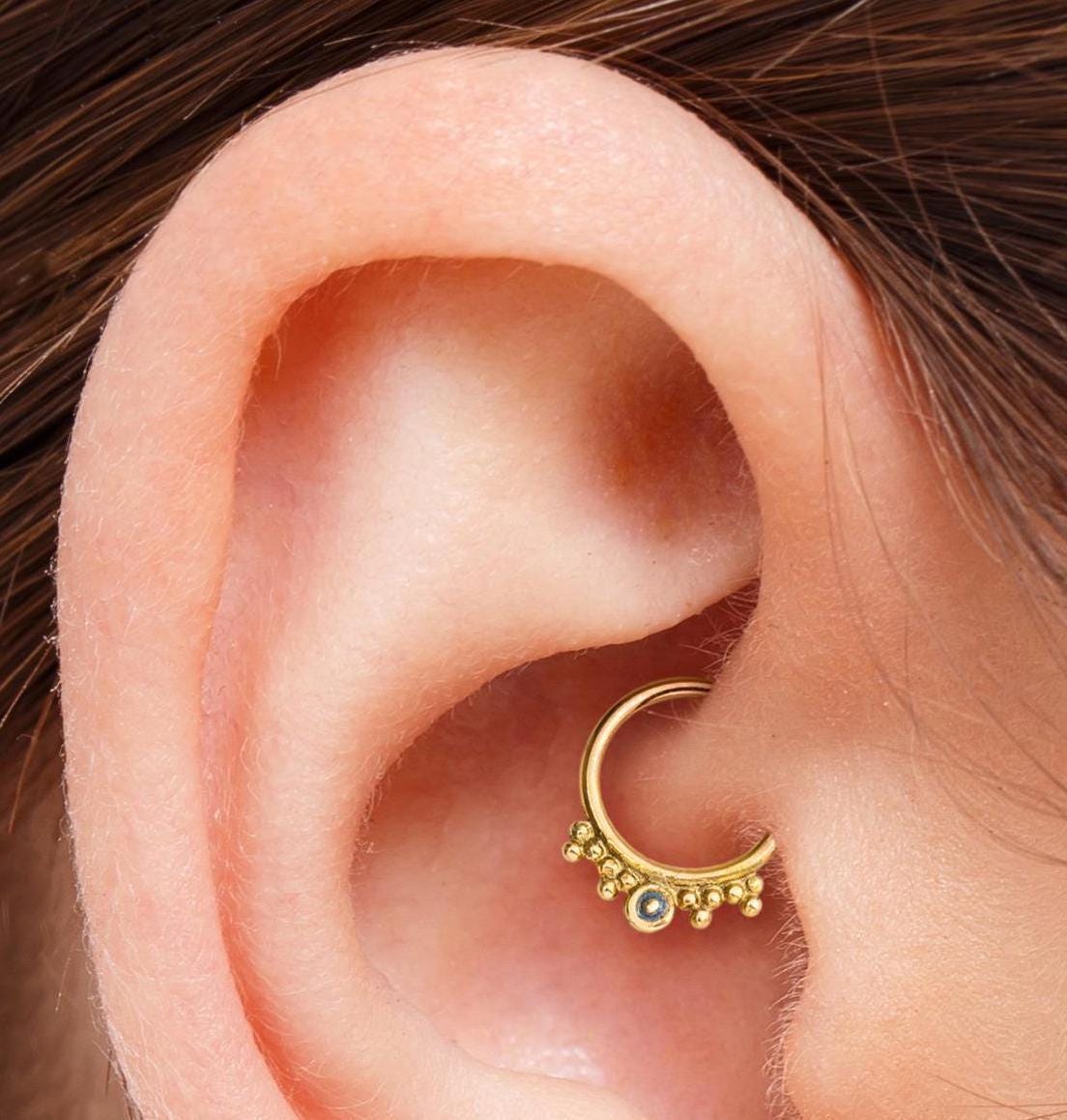 Daith Cartilage Ring: A gold hoop earring with a small blue gemstone is visible in the ear.