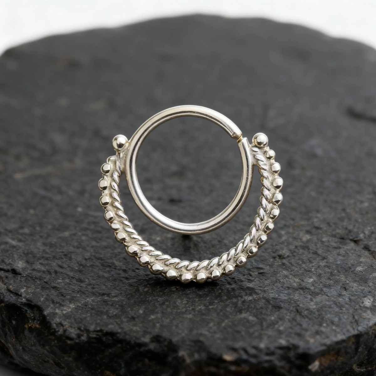 A silver-colored metal ring with a twisted design, resting on a dark surface.