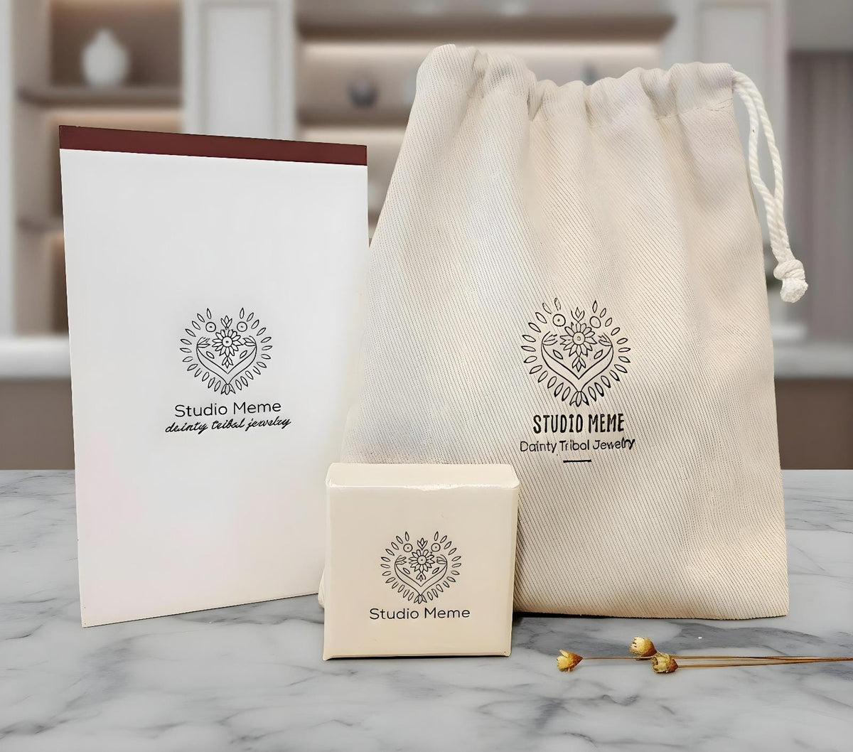 a set of jewelry items, including a white paper bag, a small box, and a white cloth bag, all with the Studio Meme logo printed on them.