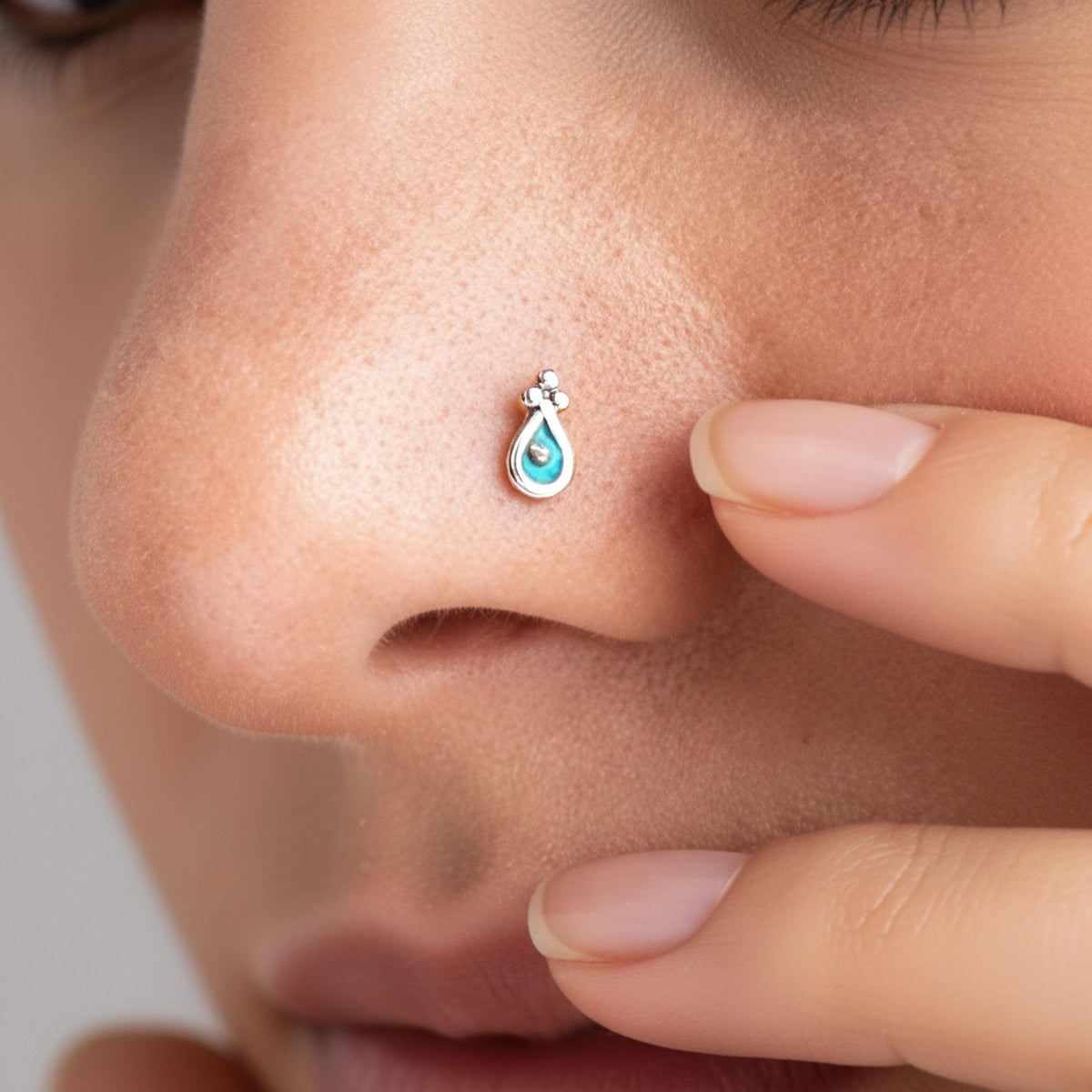 A close-up of a person's nose with a small, delicate nose ring featuring a blue gemstone.