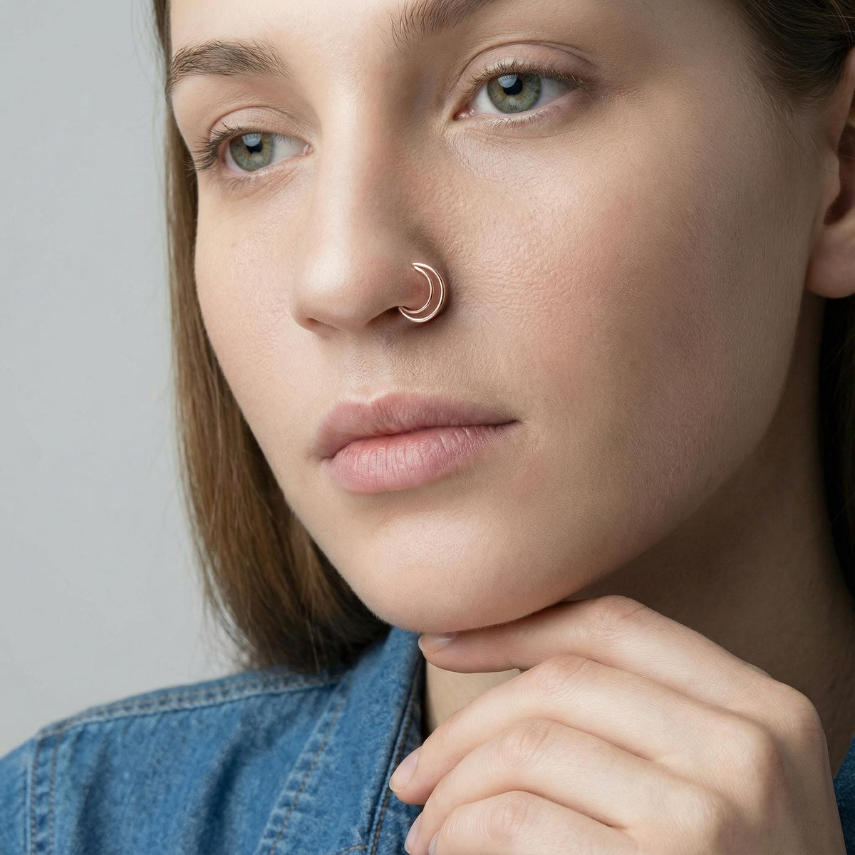 A close-up portrait of a woman with a nose ring, wearing a denim jacket.
