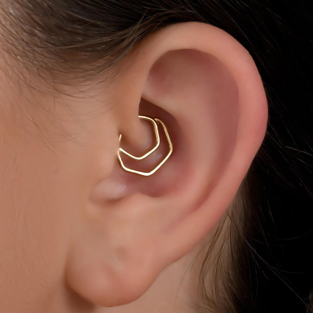 Daith Earring: A close-up view of a person's ear with a gold-colored hexagonal earring inserted.