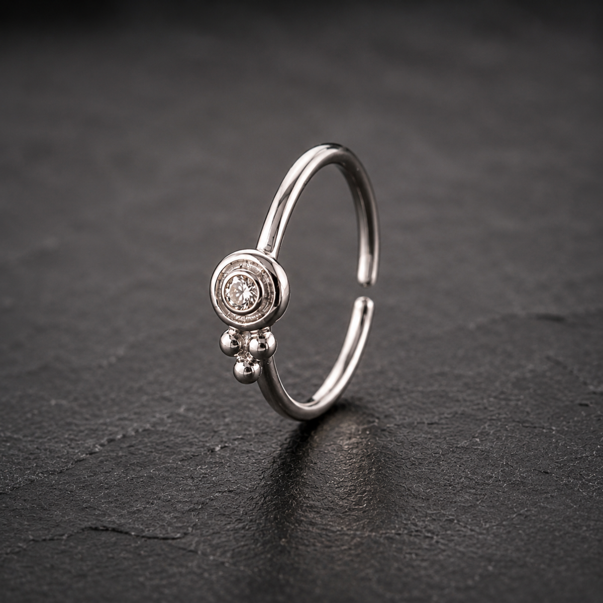 A silver ring with a small diamond in the center is displayed against a dark background.