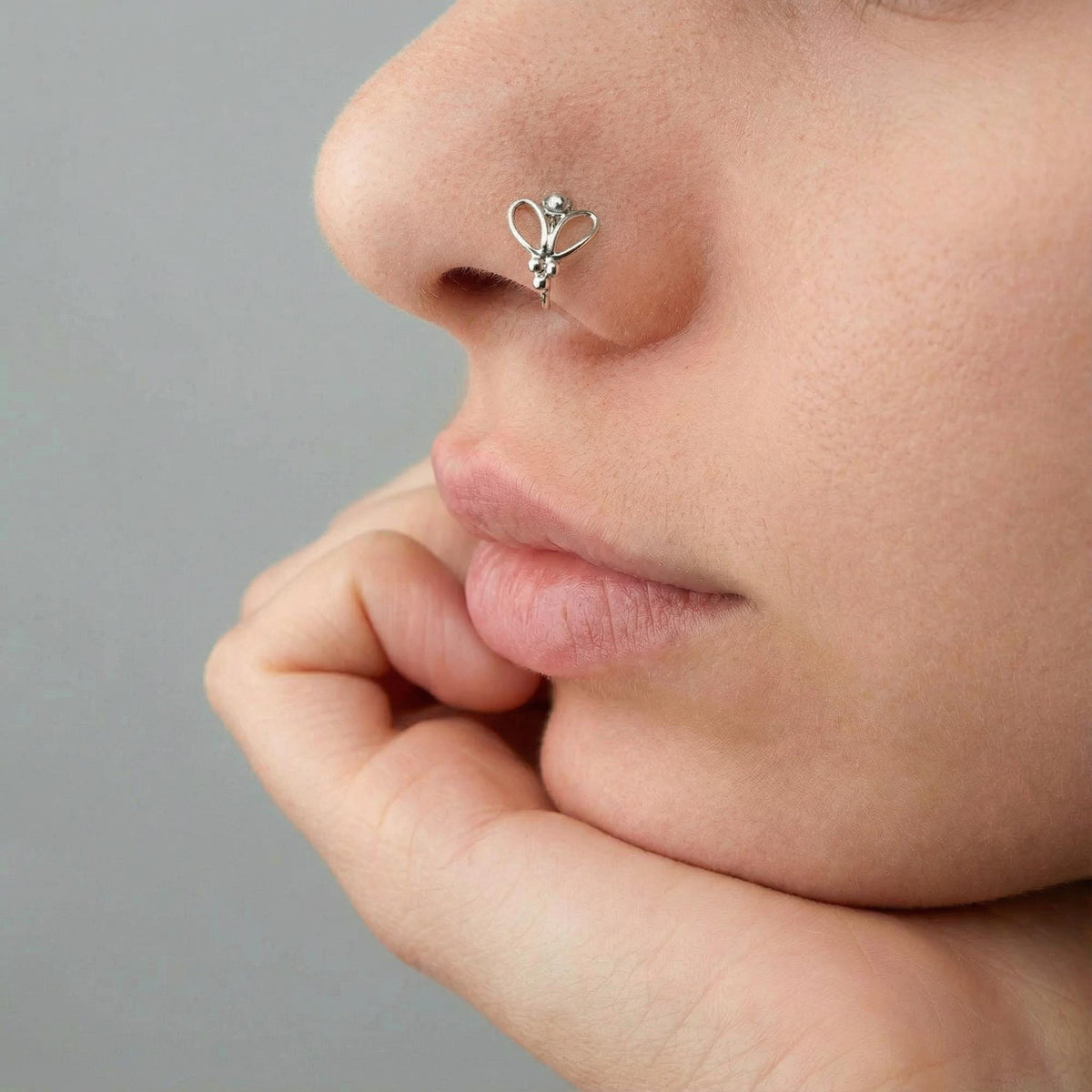 A close-up of a person's face, focusing on their nose and chin area. The person is wearing a silver nose ring with a floral design.