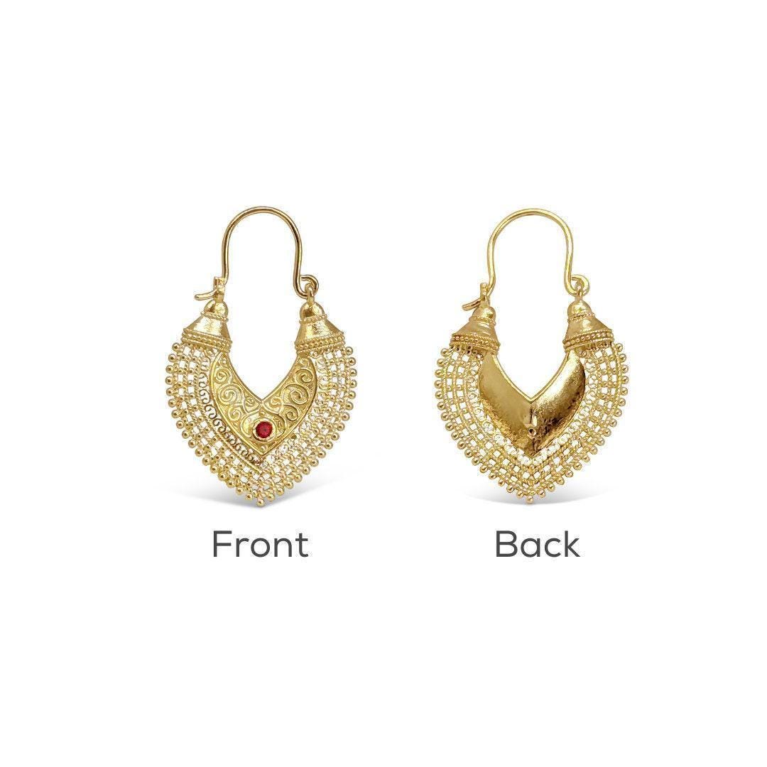 two gold earrings with intricate designs, one with a red gemstone and the other with a heart-shaped design.
