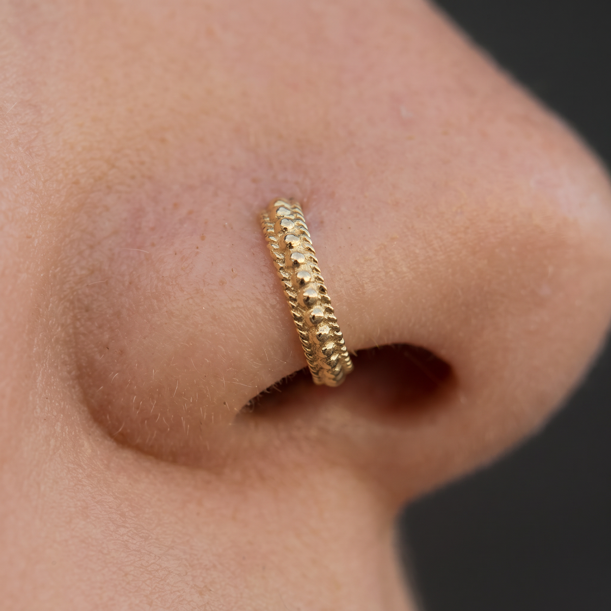 A close-up of a gold nose ring on a person's nose.