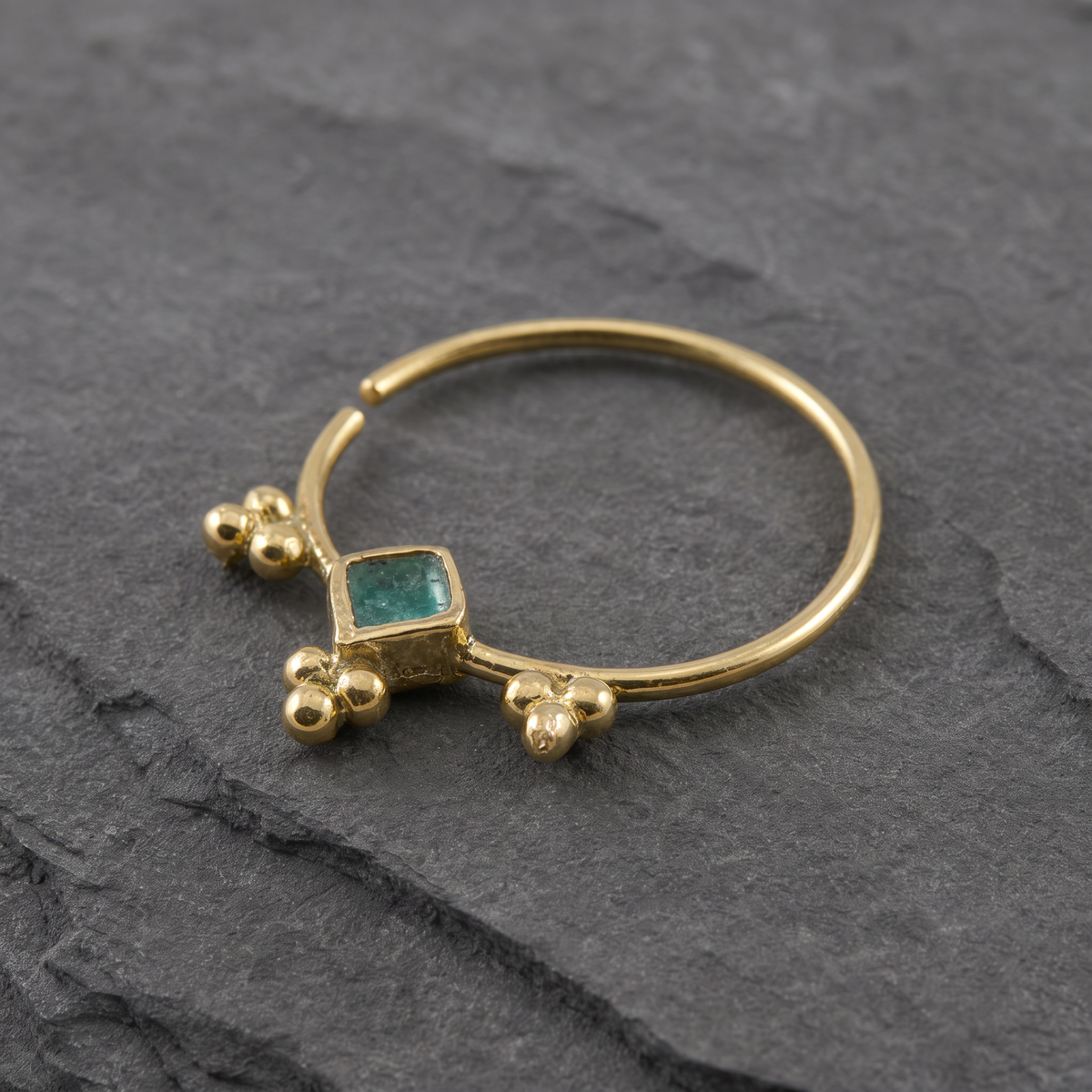 A gold ring with a green gemstone is displayed on a gray surface.
