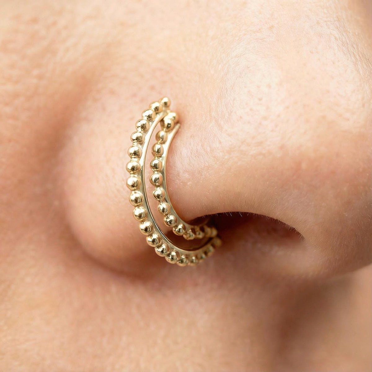 A close-up of a person's nose with a gold-colored metal nose ring.