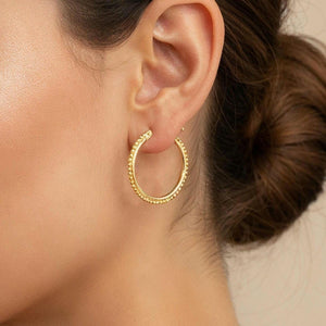 A close-up portrait of a woman with dark hair, wearing gold hoop earrings.