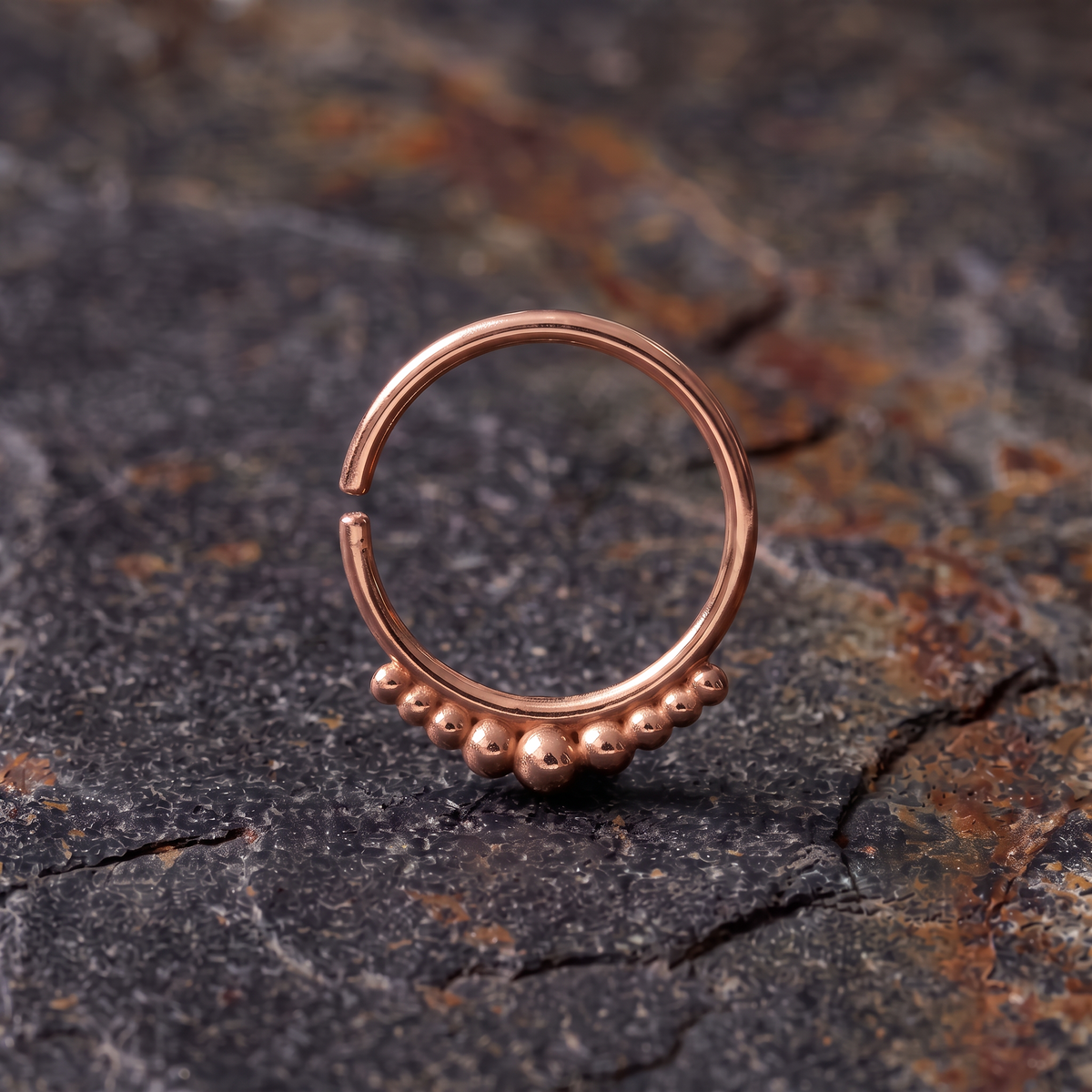 A copper-colored metal ring with a row of small balls or beads on the surface it rests on.