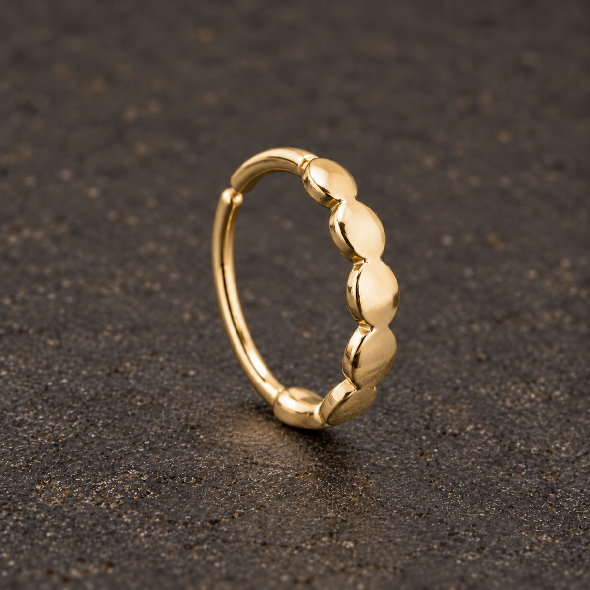 A gold ring with a row of small, round stones or dots on the surface it is resting on.