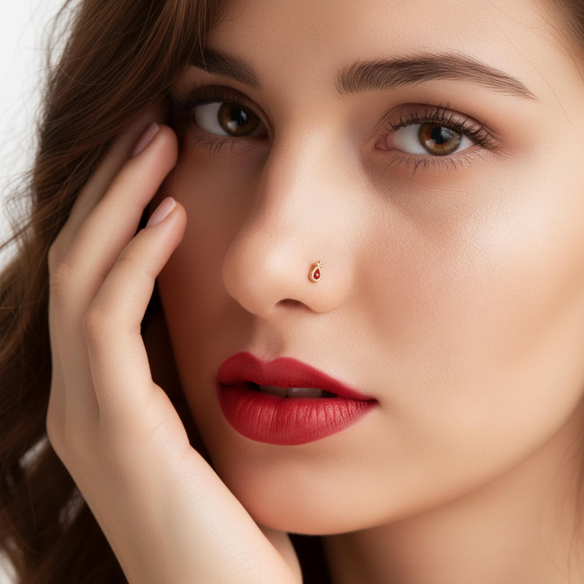 A close-up portrait of a woman with brown hair and red lipstick, looking directly at the camera with her hand on her face.