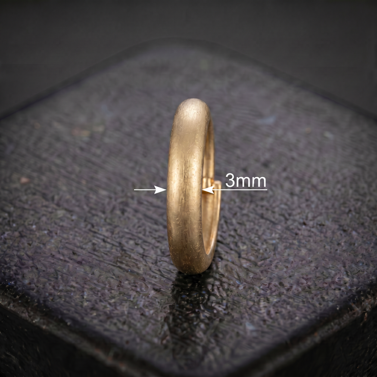 A gold ring with a 3mm measurement is shown on a black surface.