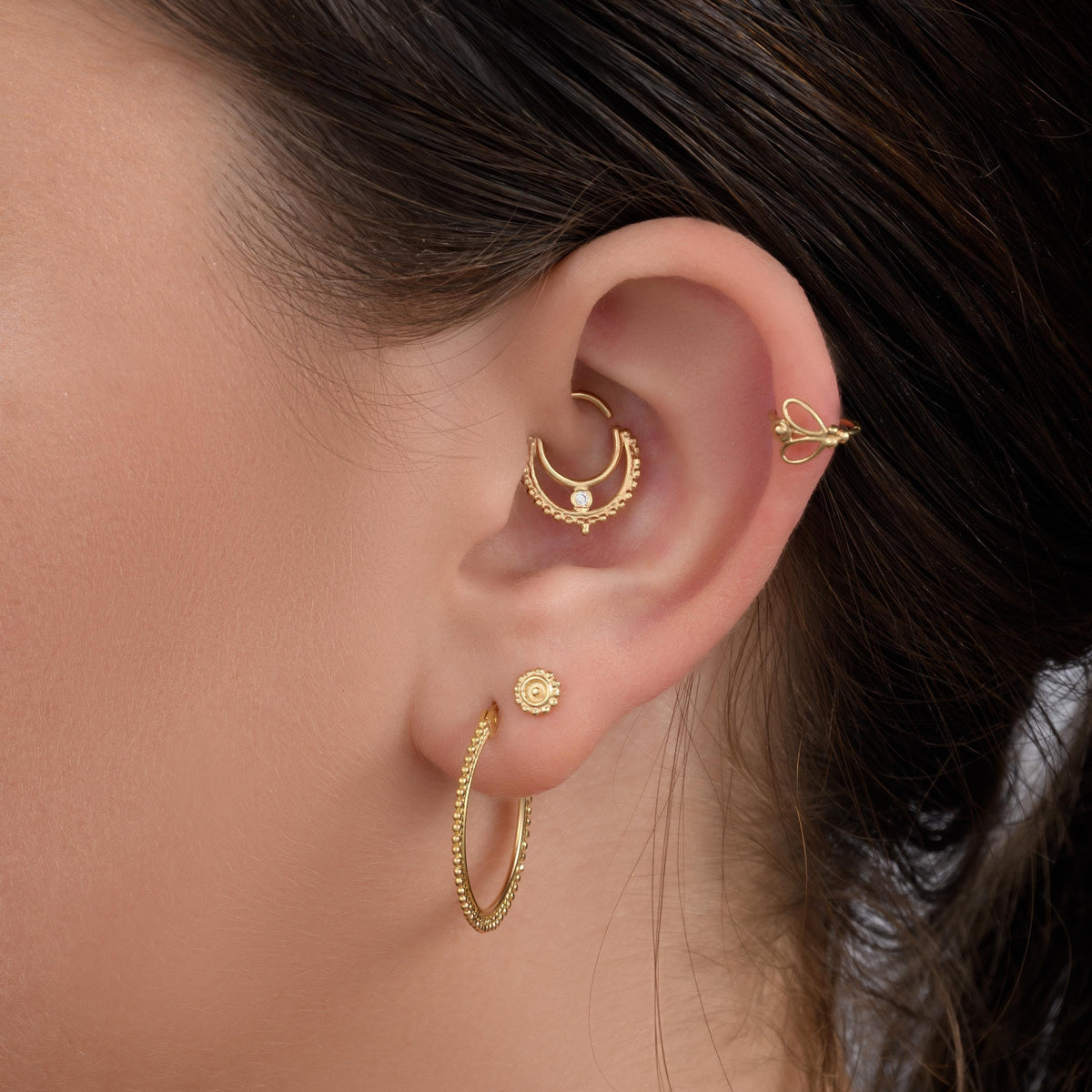 A close-up of a person's ear adorned with multiple gold earrings, including hoop earrings and a piercing.