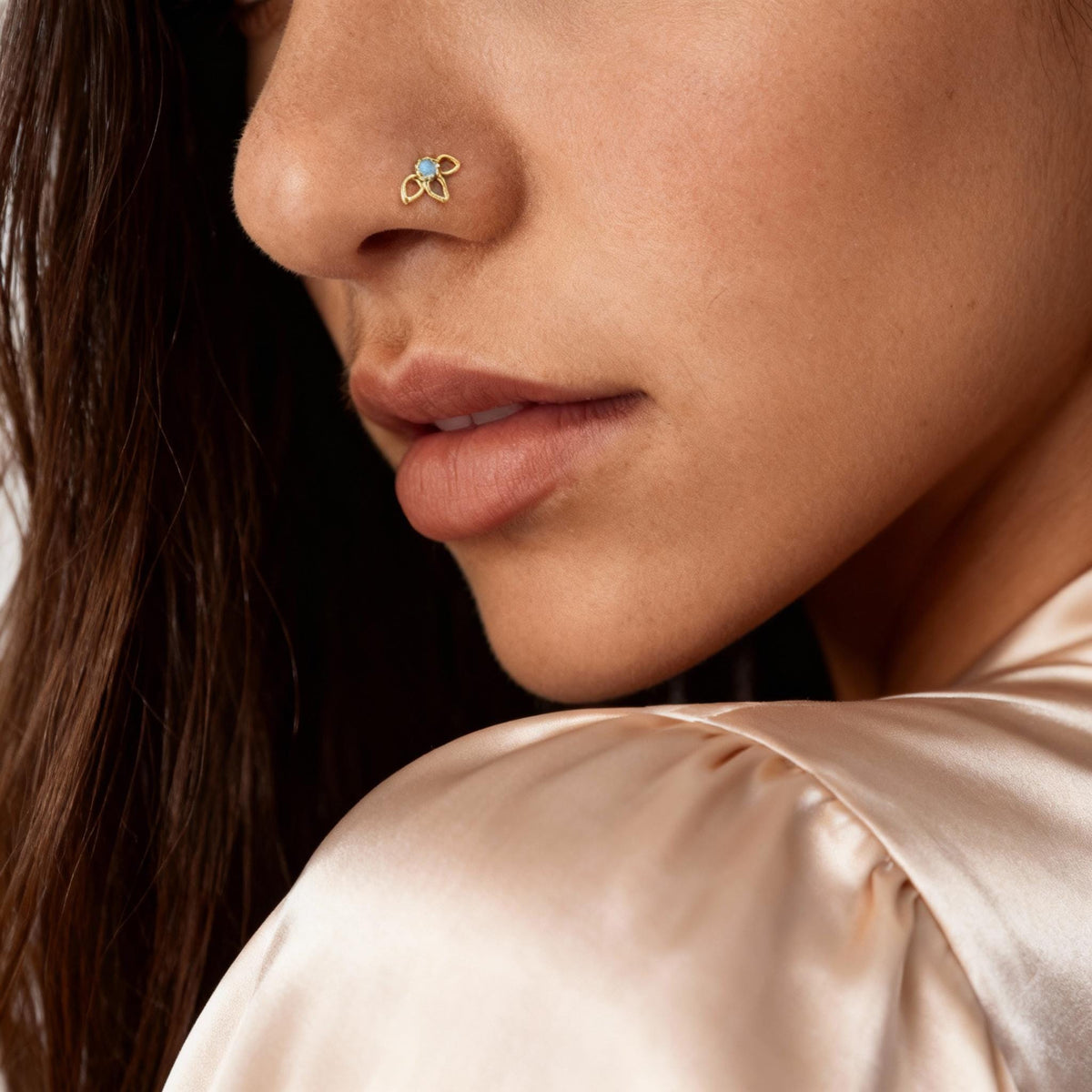 A close-up of a woman's face, focusing on her nose and chin, with a gold nose ring and a puffed-up cream-colored blouse.