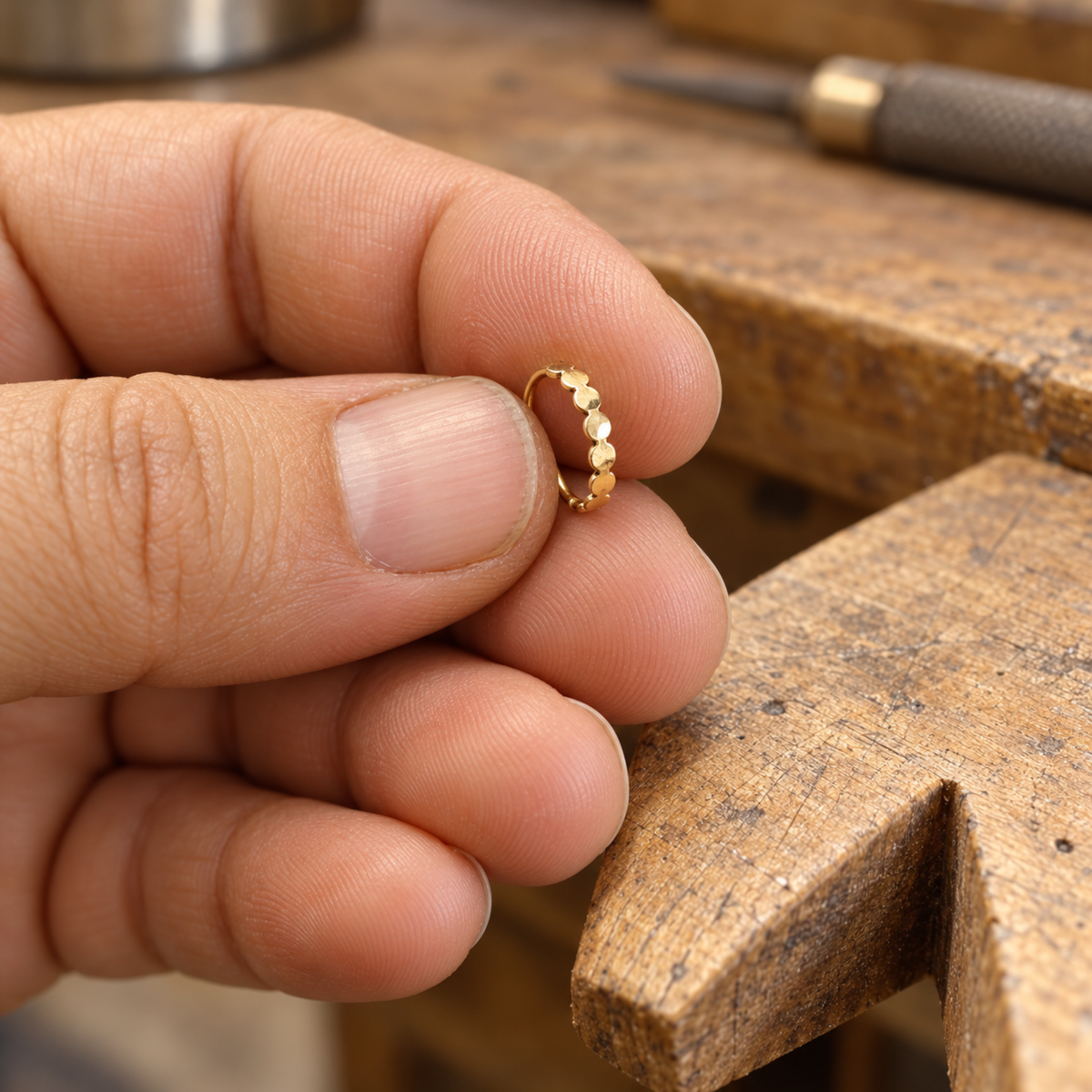 A person's hand is holding a small gold ring with a row of small stones on it, placed on a wooden surface.