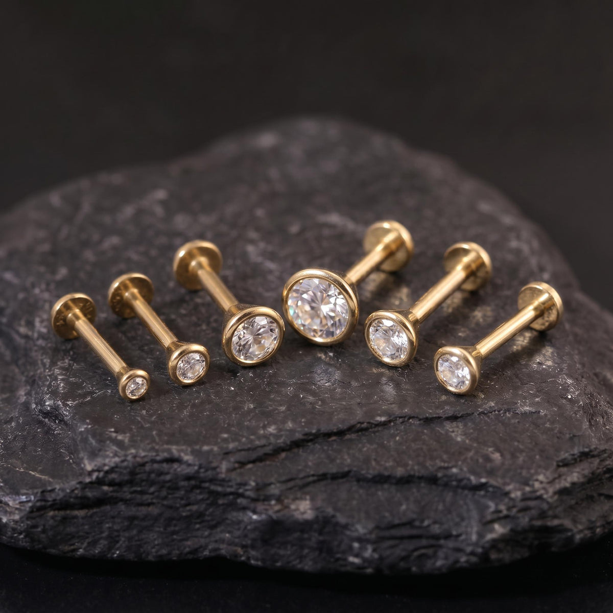 A collection of gold-colored diamond-encrusted earrings is displayed on a dark surface, likely a rock or stone.