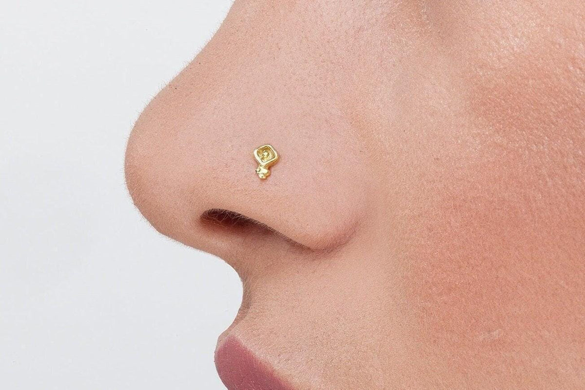A close-up of a person's nose with a small gold-colored nose stud or earring attached.