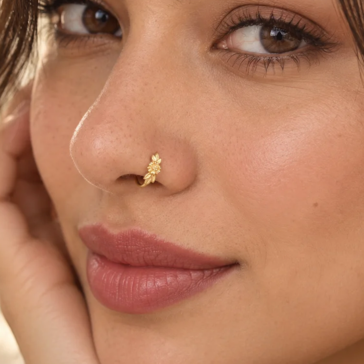 A close-up of a woman's face, focusing on her nose and lips. She is wearing a gold nose ring with a floral design.