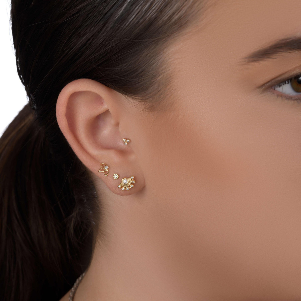 a close-up view of a person's ear adorned with several gold earrings.