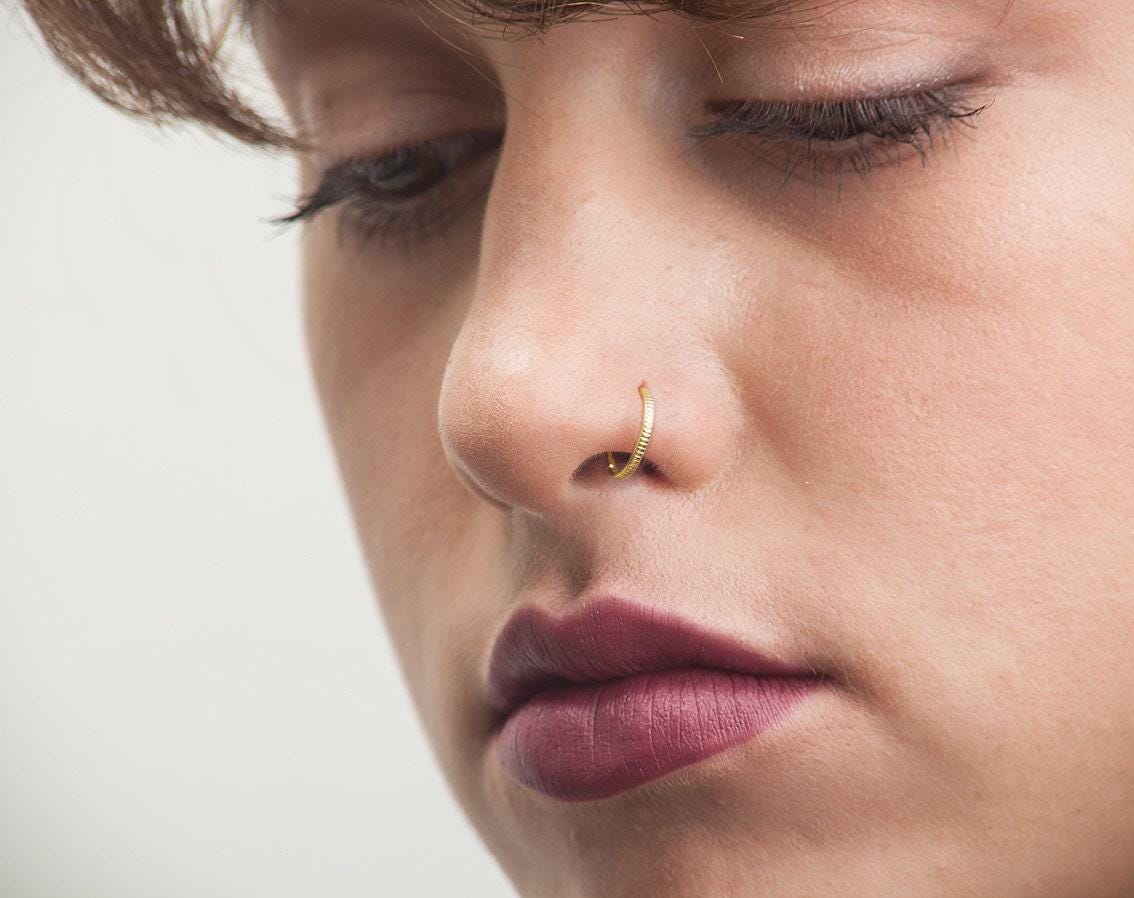 A close-up of a woman's face, focusing on her nose and lips, with a gold nose ring visible.