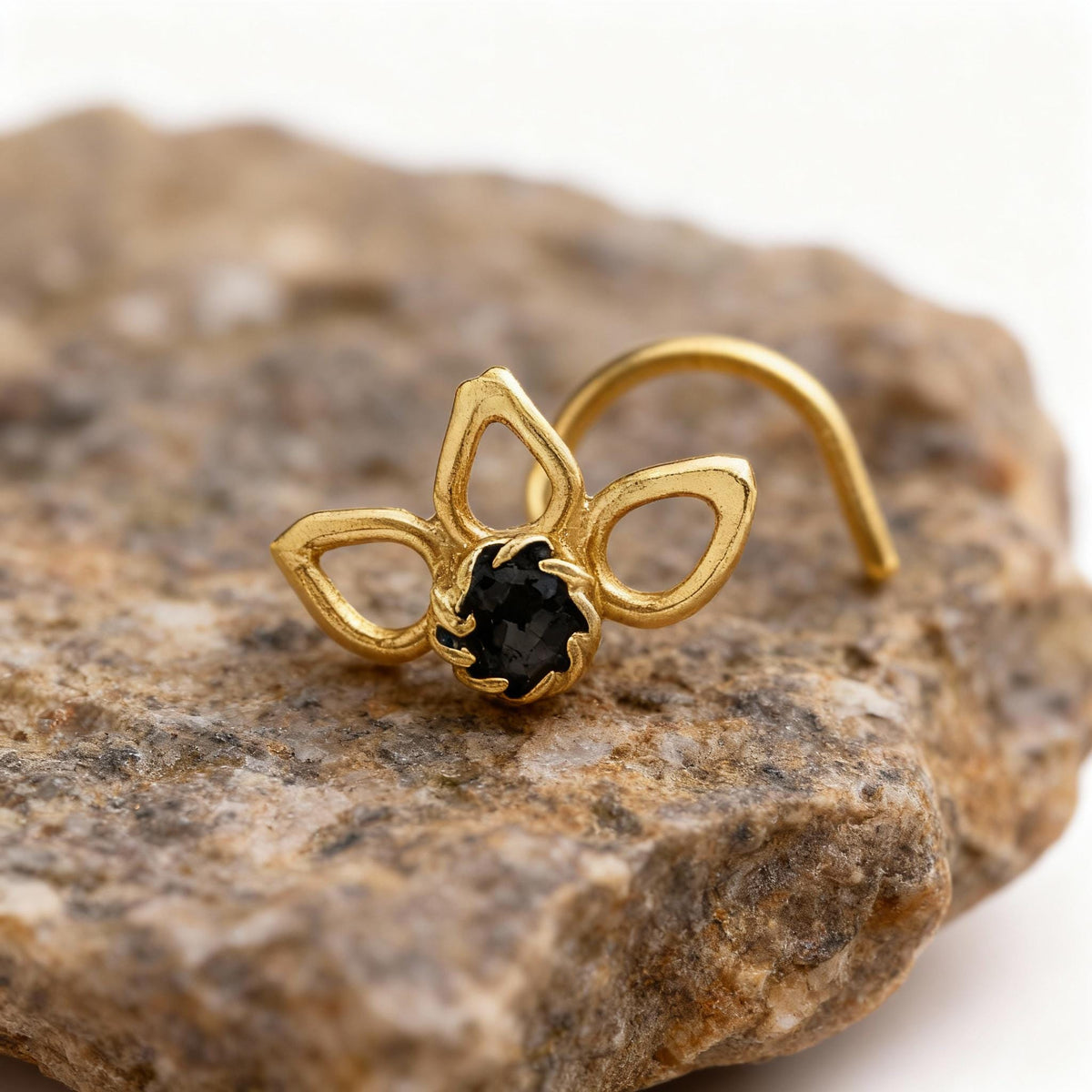 A gold-colored nose ring with a black gemstone is resting on a rock.