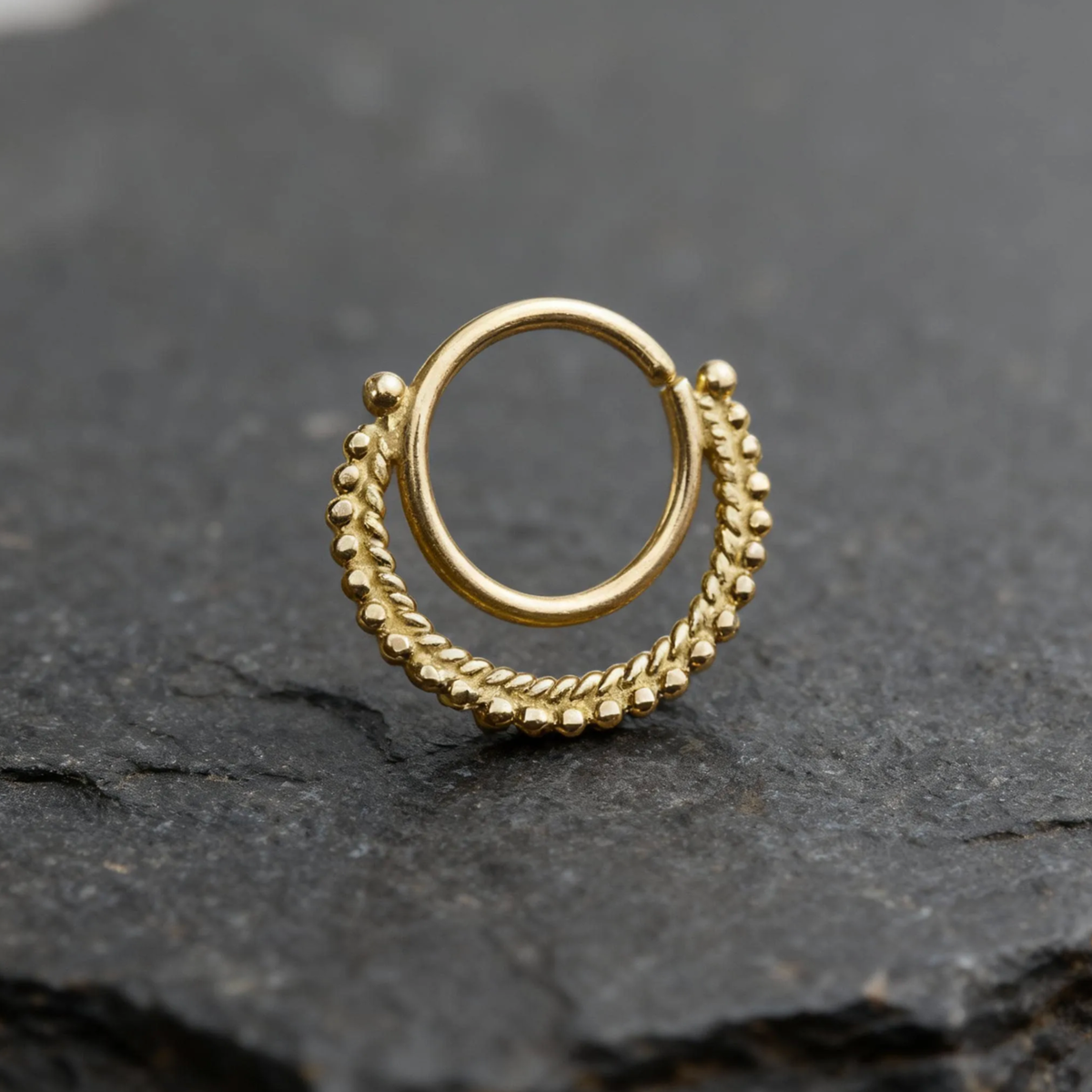 A gold-colored metal ring with a twisted design sits on a dark surface.