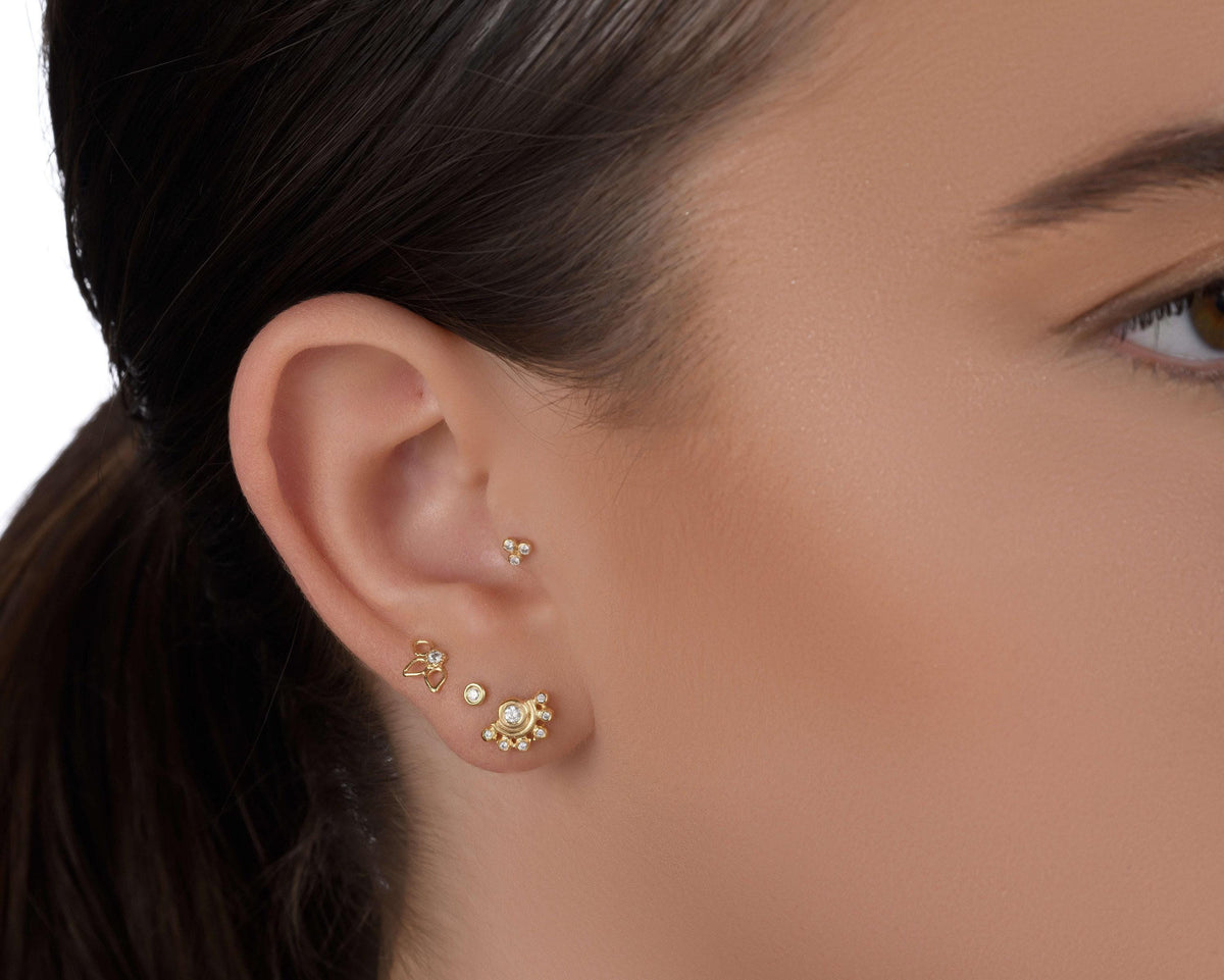 A close-up of a person's ear adorned with multiple gold earrings, including a pair of dangling earrings and a stud earring.