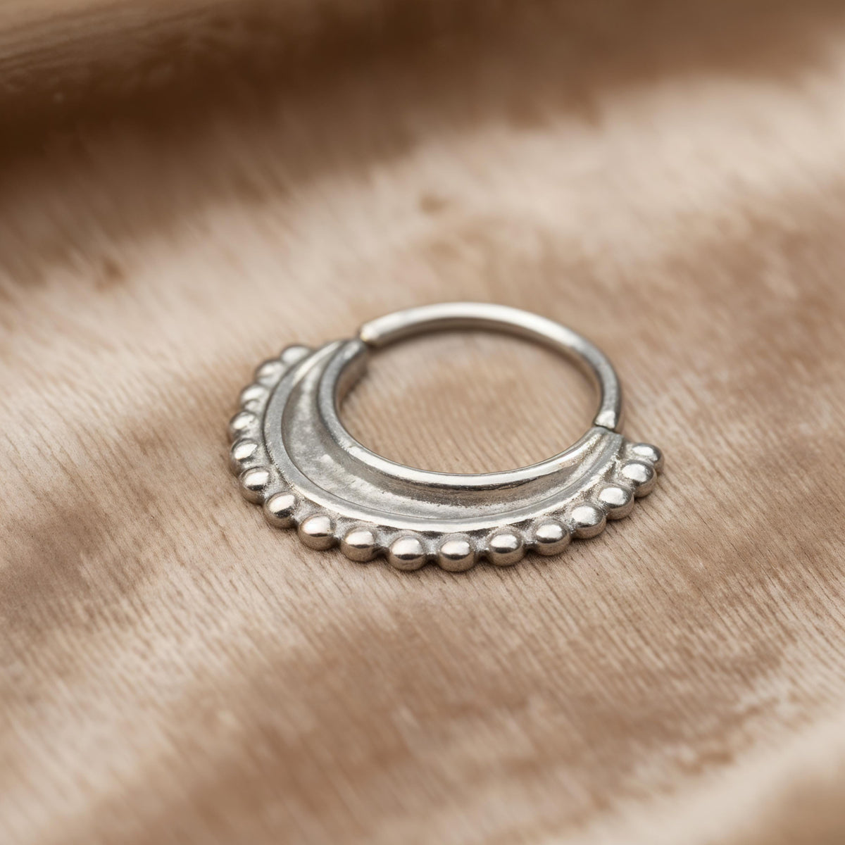 Nose Hoop Jewelry: A silver-colored metal ring with a decorative design sits on a textured fabric surface.