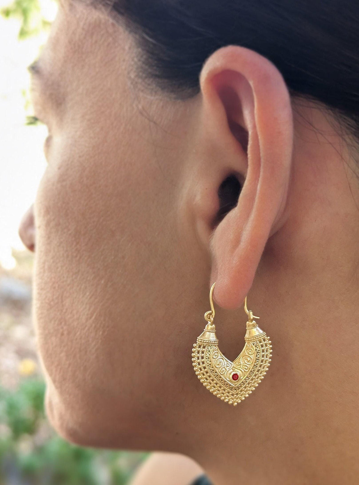 A close-up of a person's face, focusing on their ear and the gold earring with a red gemstone.